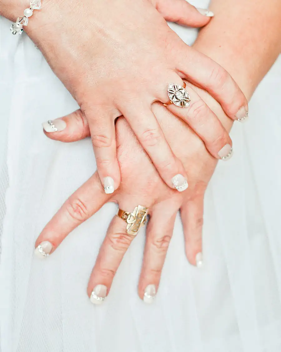 Deux mains de femme croisées, ornées de bagues en or et en argent, sur un tissu blanc.