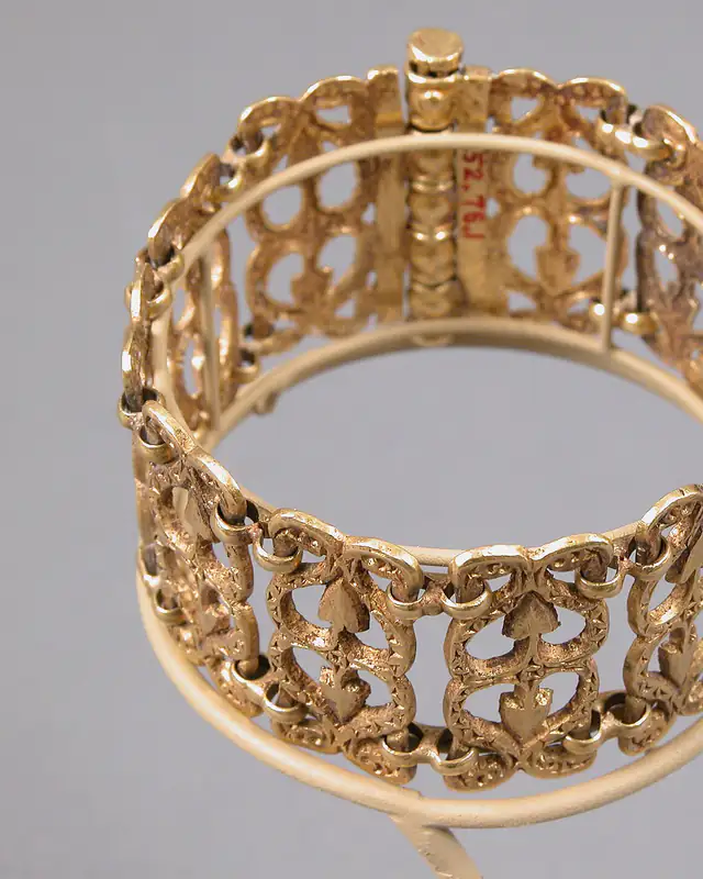 Un bracelet manchette en or ciselé, posé sur un support.