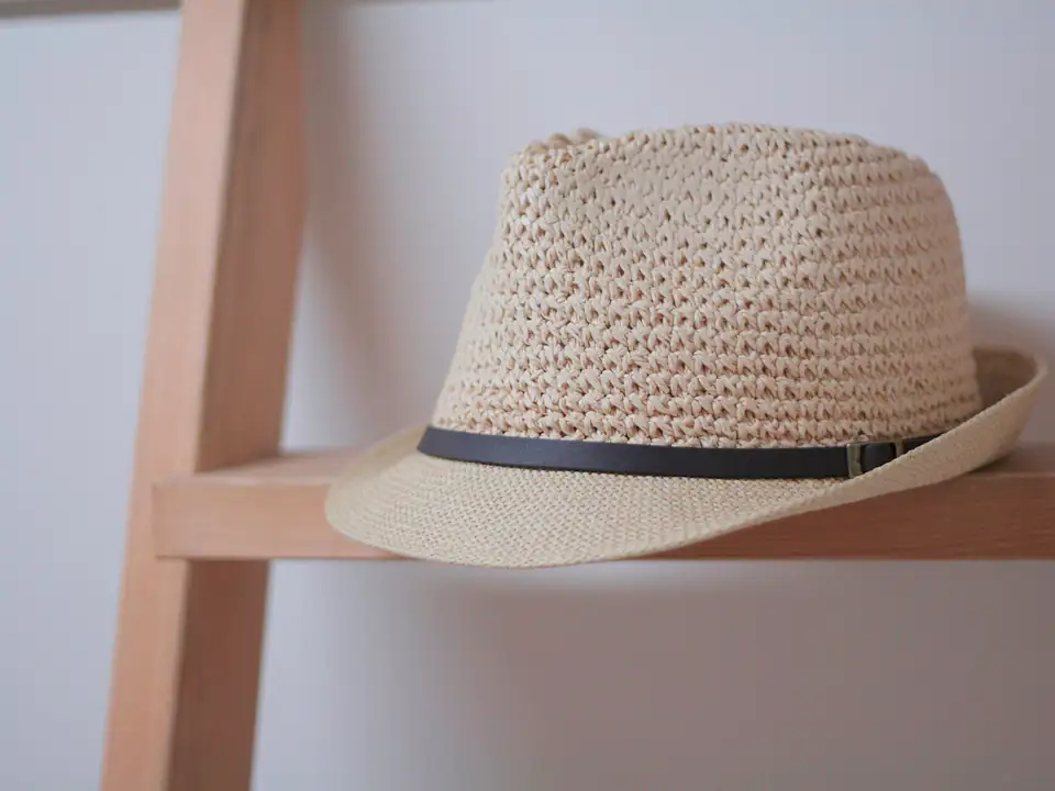 Un chapeau de paille à ruban noir posé sur une étagère en bois clair.