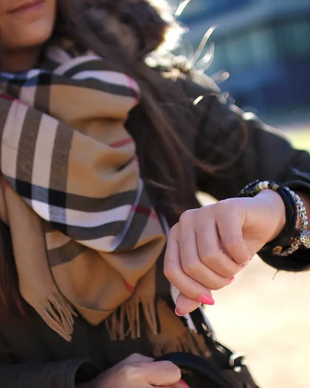 Une femme en écharpe à carreaux regarde sa montre, des bracelets au poignet.