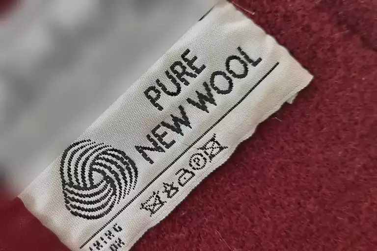 Étiquette tissée cousue dans un manteau rouge, avec la mention « Pure new wool », le logo de la laine et les symboles d’entretien.