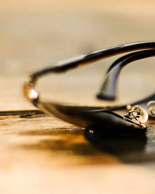 Des lunettes de soleil à monture noire et branches dorées, sur une table en bois au soleil.